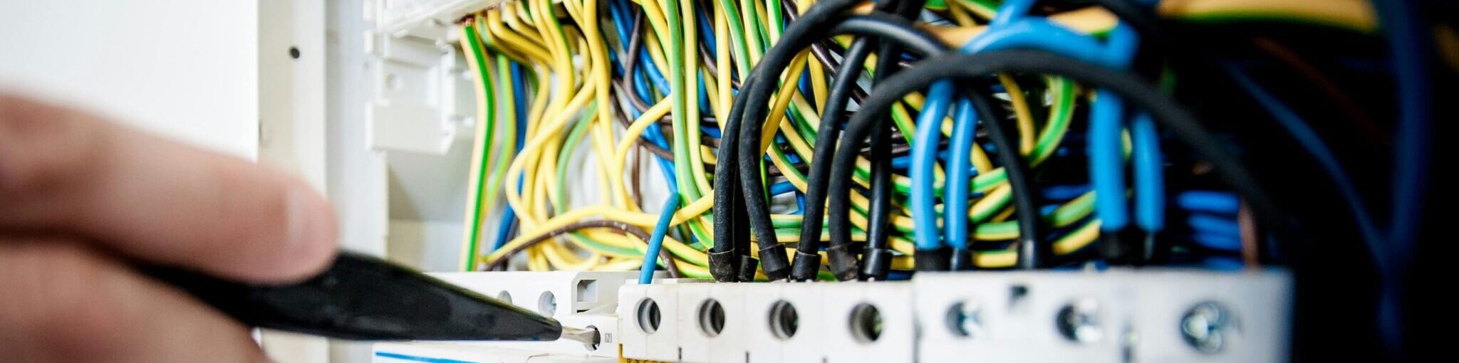 Hand of electrician working on a circuit breaker panel with colorful wires, ensuring safe electrical connections.
